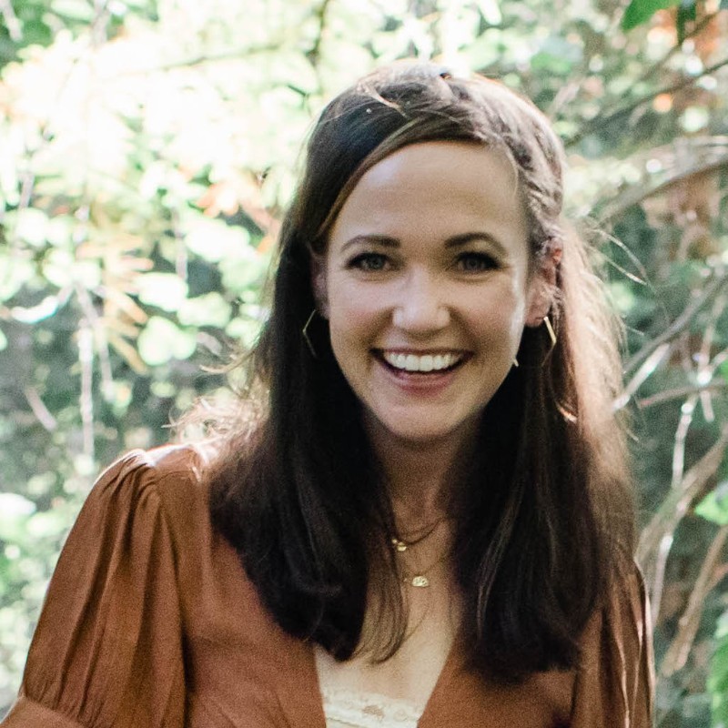 headshot of megan arnett wearing a brown shirt with a background of trees and leaves behind